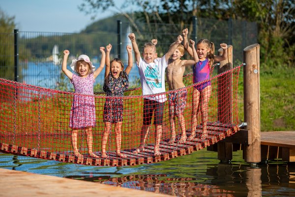 Fünf Kinder stehen auf einer Hängeseilbrücke und strecken die Arme in die Luft.