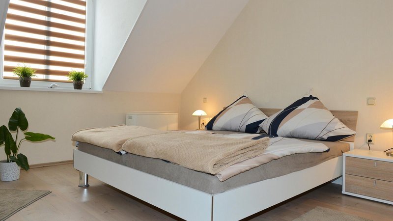 Schlafzimmer mit bezogenem Bett und Bettwäsche, einem Nachttisch und einem Fenster