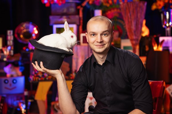 Ein Mann hält einen Hund in der Hand. In dem Hut befindet sich ein weißer Hase.