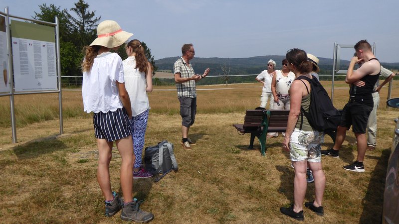 Eine Menschengruppe an Touristen steht auf einem Feld, auf dem sich eine Infotafel zu einer Sehenswürdigkeit befindet und lauscht gebannt dem Gästeführer