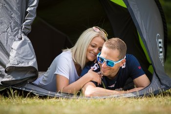 Eine Frau und ein Mann liegen bäuchlings in einem Zelt, schauen aus dem Zelt heraus und die Frau kuschelt sich an den Mann.