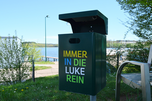 Grüner Mülleimer mit der bunten Aufschrift "Immer in die Luke rein"