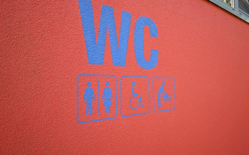 Die Aufschrift WC und Pictogramme in blau auf einem roten Hintergrund