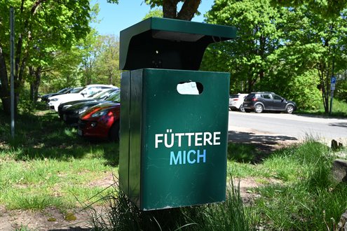 Grüner Mülleimer mit der bunten Aufschrift "Füttere mich"