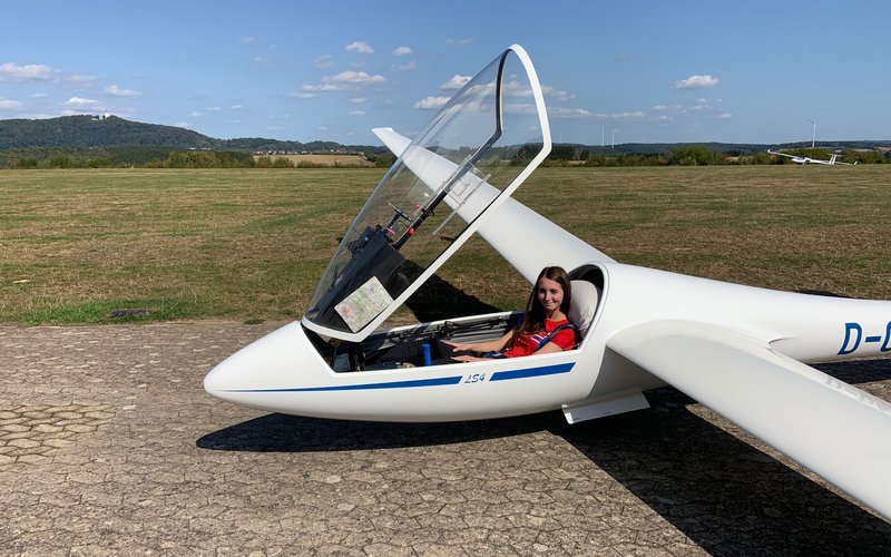 Auf dem Segelflugplatz in Marpingen steht ein weißes Segelflugzeug, das die Schutzscheibe geöffnet hat. Eine Frau sitz darin. 