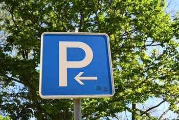 Ein blaues Parkplatzschild mit einem weißen P und einem weißen Pfeil nach links