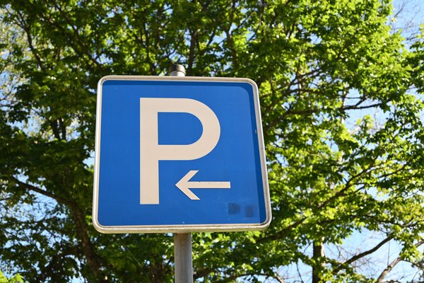 Ein blaues Parkplatzschild mit einem weißen P und einem weißen Pfeil nach links