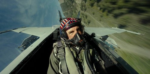Maverick trägt einen Helm und eine Atemmaske und fliegt einen Jet, der sich in der Luft befindet.