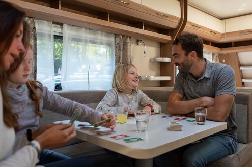 In der Sitzecke eines Mietwohnwagens des Campingplatzes Bostalsee ist eine Familie zu sehen, die zusammen Karten spielt.