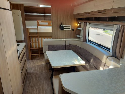Das Foto zeigt eine Innenaufnahme eines Mietwohnwagens, insbesondere eine Sitzecke und Kochnische.