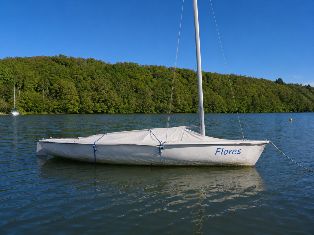 Ein Segelboot mit dem Namen "Flores" liegt still auf dem Wasser. Das Segel ist nicht ausgefahren.