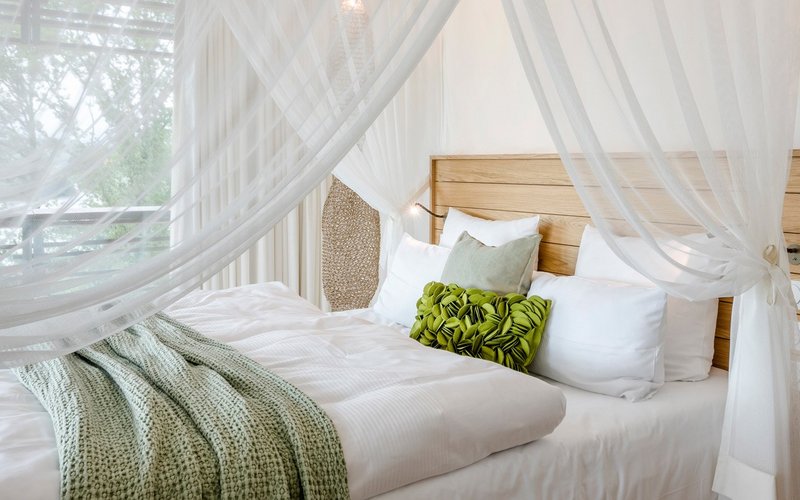 Ein gemütlich beleuchtetes Zimmer mit einem großen Himmelbett mit einer grünen Tagesdecke und vielen Kissen darauf.