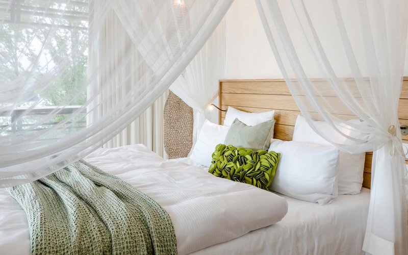 Ein gemütlich beleuchtetes Zimmer mit einem großen Himmelbett mit einer grünen Tagesdecke und vielen Kissen darauf.