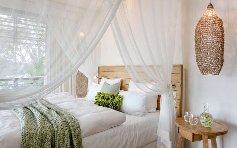 Ein gemütlich beleuchtetes Zimmer mit einem großen Himmelbett mit einer grünen Tagesdecke und vielen Kissen darauf.