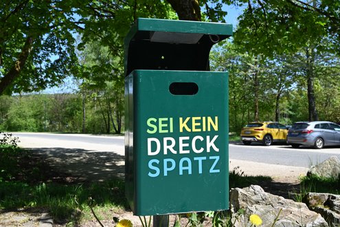 Grüner Mülleimer mit der bunten Aufschrift "Sei kein Dreckspatz"