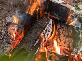 Vor einem Mietwohnwagen des Campingplatzes Bostalsee hat es sich ein Pärchen mit einem Getränk am Grillfeuer, über dem ein Schwenker hängt, gemütlich gemacht.