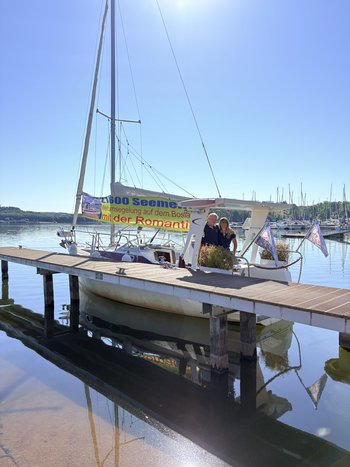 Ein Mann und eine Frau stehen auf einem Segelboot, das im Hafen liegt